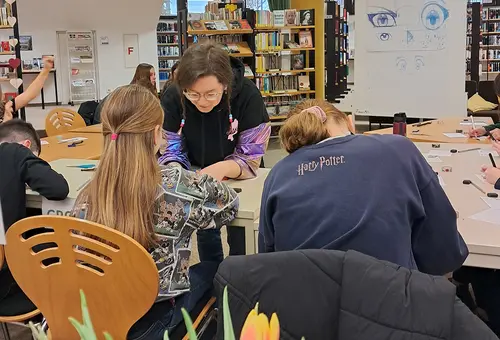 Eine Frau hilft zwei Mädchen beim Zeichnen.