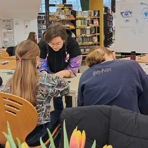 Eine Frau hilft zwei Mädchen beim Zeichnen.