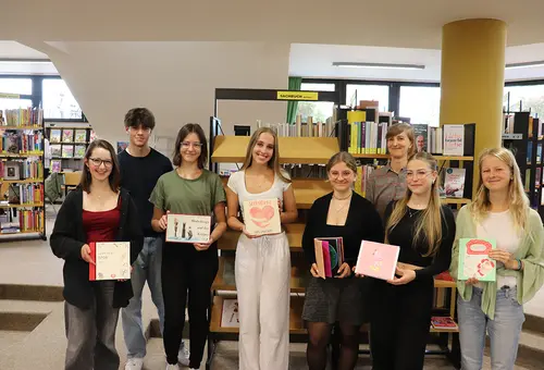 Ein Schüler und sechs Schülerinnen präsentieren ihre Bücher. Im Hintergrund steht die Lehrerin.