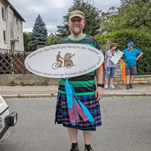 Ein Mann im Kilt hält ein Schild mit der Aufschrift "Jeder hat das Recht auf Wind in den Haaren - in Oberasbach lassen sich die Senioren mit der ERIKA fahren!