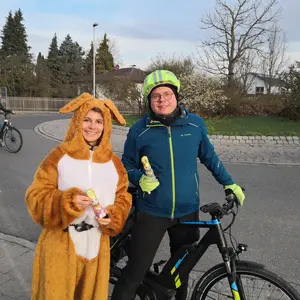 Eine Frau im Plüschhasenkostüm mit einer Frau mit Fahrradhelm auf einem Rad. Beide halten Schokohasen in den Händen.