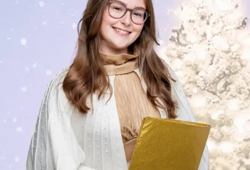 Das Oberasbacher Christkind mit einem goldenen Buch in der Hand vor einem hell leuchtenden Weihnachtsbaum.