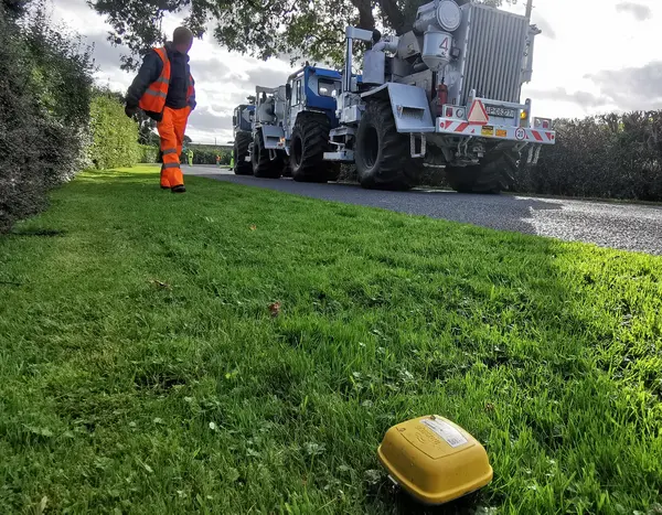 gelbe kleine Box auf grünem Rasen; im Hintergrund ein großer Lkw, ein so genannter Vibrottrurck