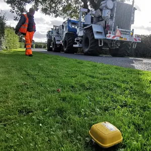 gelbe kleine Box auf grünem Rasen; im Hintergrund ein großer Lkw, ein so genannter Vibrottrurck