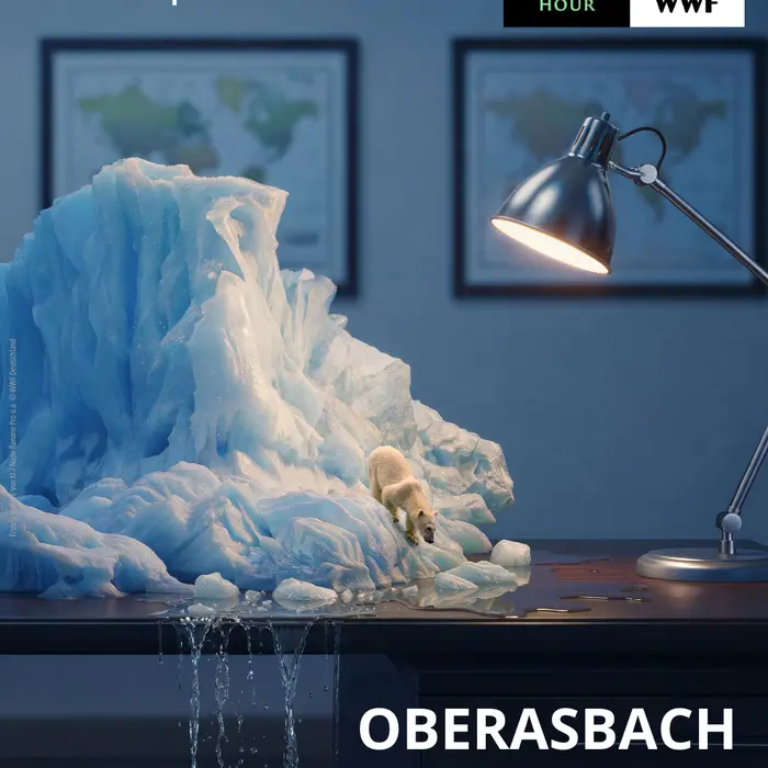 Auf einem Schreibtisch steht ein Eisberg mit einem Eisbär. Durch die Schreibtischlampe schmilzt das Eis. Titel Oberasbach macht's aus. Oben Logo WWF
