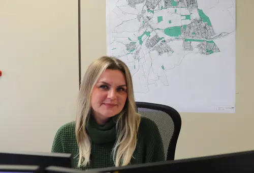 Katharina Geiger am Schreibtisch, Karte im Hintergrund 