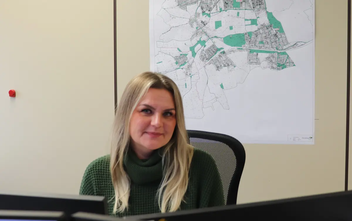 Katharina Geiger am Schreibtisch, Karte im Hintergrund 