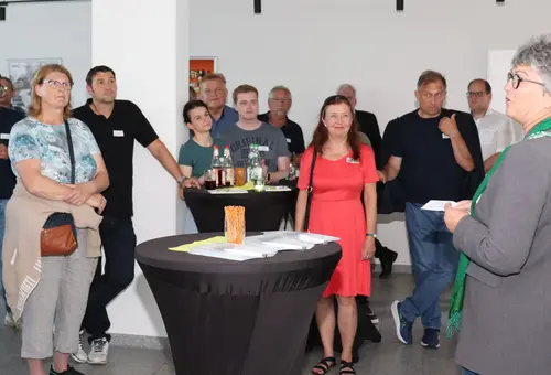 eine Gruppe von Männer und Frauen an Stehtischen. Vorn rechts Birgit Huber, die zu ihnen spricht. 