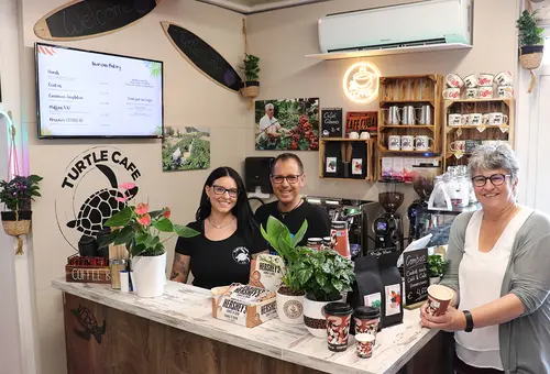 Ein Mann und eine FRau stehen hintr einem Tresen, die Bürgermeisterin mit einer Tasse Kaffee vor dem Tresen.