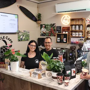 Ein Mann und eine FRau stehen hintr einem Tresen, die Bürgermeisterin mit einer Tasse Kaffee vor dem Tresen.