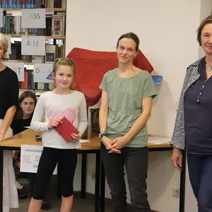 Ein Kind bei der Preisübergabe. Im Hintergrund drei Frauen vom Büchereiteam.