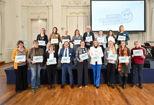 17 Personen im Gruppenbild, jeder hält das Logo in der Hand