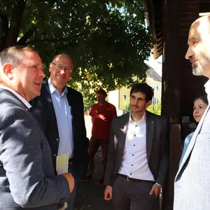 Mehrere Männer stehen unter einem Baum vor der Scheune und unterhalten sich.