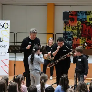 Zwei Männer erklären zwei Kindern die Mundstücke. Im Hintergrund die anderen Musiker.