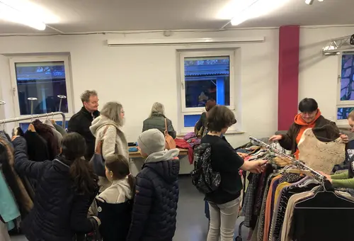 Menschen allen Alters betrachten Kleidung auf Kleiderständern im Jugendhaus. 
