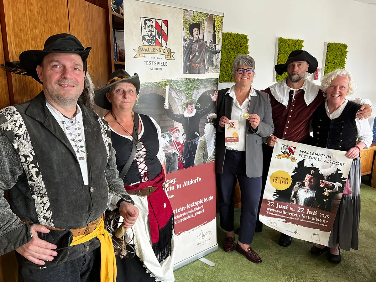 Zwei Männer und zwei Frauen in historischer Tracht präsentieren Birgit Huber ihre Einladung zu den Festspielen.