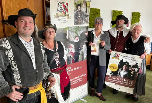 Zwei Männer und zwei Frauen in historischer Tracht präsentieren Birgit Huber ihre Einladung zu den Festspielen.