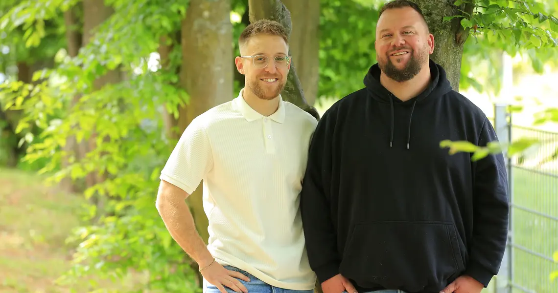 zwei Männer in Freizeitkleidung in vor einem grünen Baum 