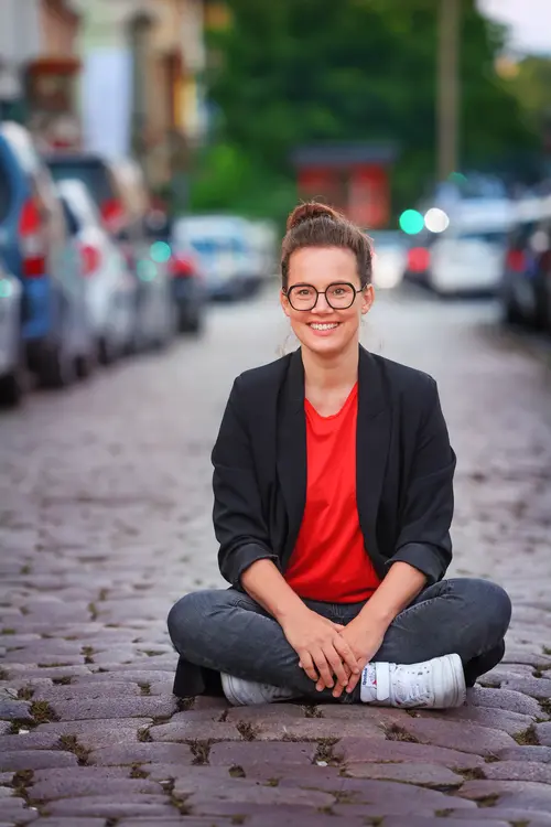 Katja Diehel sitzt auf dem Kopfsteinpflaster einer Straße. Im Hintergrund parkende Autos. 
