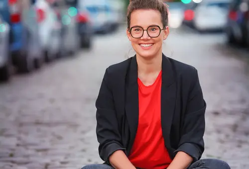 Katja Diehel sitzt auf dem Kopfsteinpflaster einer Straße. Im Hintergrund parkende Autos. 