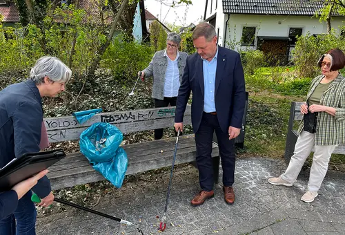 Vier Personen sammeln rund um eine Parkbank Müll auf.