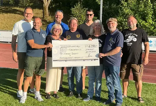 6 Männer und 3 Frauen halten auf einem Sportplatz einen großen, symbolischen Spendencheck über 6350 Euro.