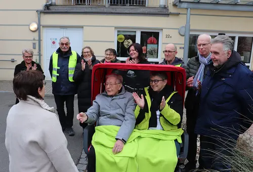 Zwei Personen in der E-Rikscha und neun umstehende Personen applaudieren.