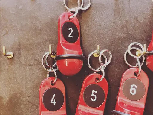 Schlüsselbrett mit Haken, an denen Schlüssel für Hotelzimmer hängen. Die Anhänger tragen die Zahlen 2, 4, 5 und 6.