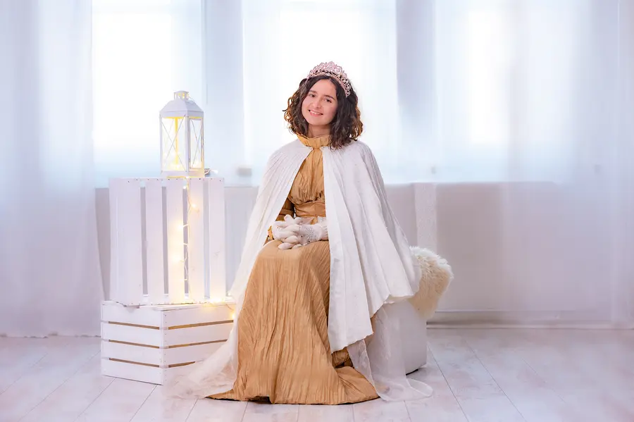 Eine junge Frau mit Christkind-Bekleidung sitzt in einem weißen Raum