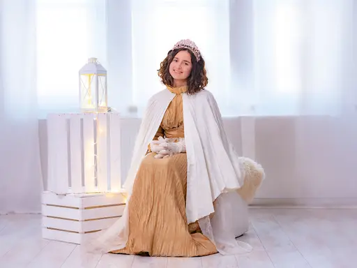 Eine junge Frau mit Christkind-Bekleidung sitzt in einem weißen Raum