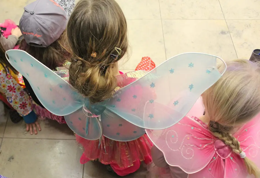 drei Kinder als Elfen oder Feen verkleidet sind von hinten im Sitzen zu sehen.