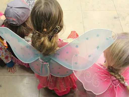 drei Kinder als Elfen oder Feen verkleidet sind von hinten im Sitzen zu sehen.