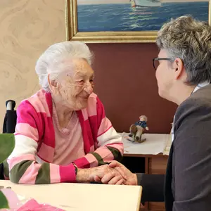 Eine Dame mittleren Alters hält die Hand einer alten Dame, beide sind in ein Gespräch vertieft