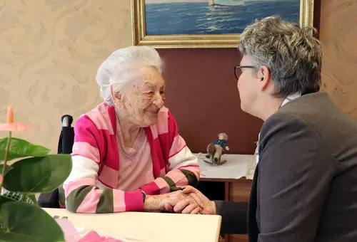 Eine Dame mittleren Alters hält die Hand einer alten Dame, beide sind in ein Gespräch vertieft