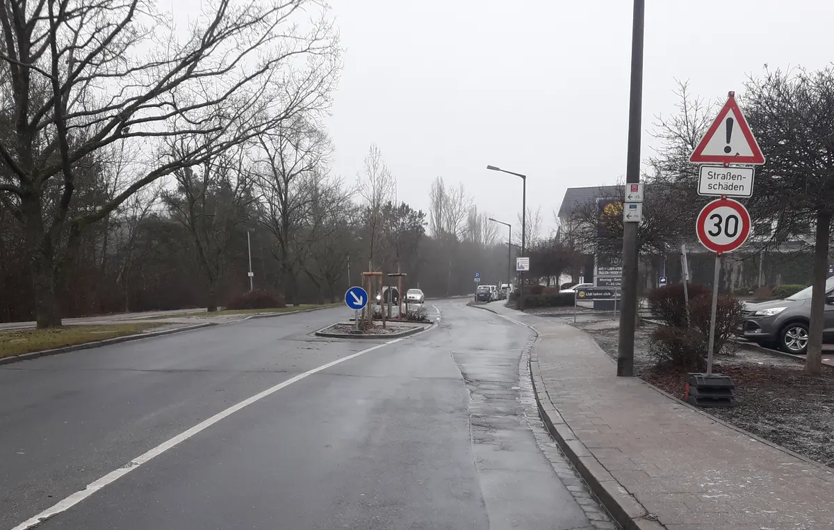 Straße mit Verkehrsinsel in der Mitte und Gehweg auf der rechten Seite
