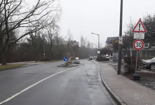 Straße mit Verkehrsinsel in der Mitte und Gehweg auf der rechten Seite