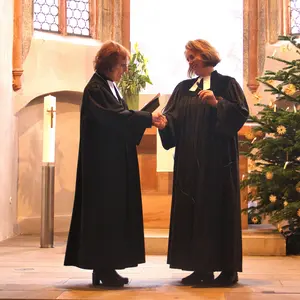 Zwei Frauen im schwarzen Talar stehen im Kirchenraum und beglückwünschen sich.