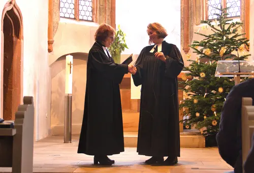 Zwei Frauen im schwarzen Talar stehen im Kirchenraum und beglückwünschen sich.