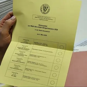 Eine Männerhand, die einen gelben Stimmzettel mit KandidatInnennamen fürs Bürgermeisteramt hält