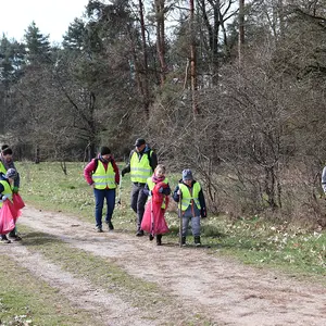 Drei Grundschulkinder mit vier Erwachsenen mit Warnwesten und Müllbeuteln auf einem Weg im Hainberg.