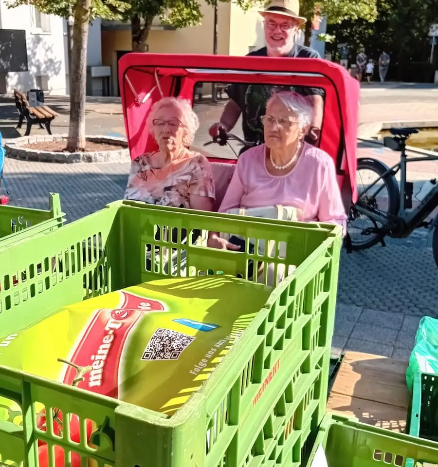 Zwei Seniorinnen sitzen in einer Fahrradrikscha und betrachten Gemüse auf dem Wochenmarkt 