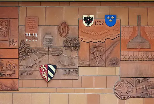 Tonrelief an der Wand mit Wappen und geschichtlichen Motiven