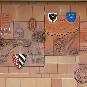 Tonrelief an der Wand mit Wappen und geschichtlichen Motiven