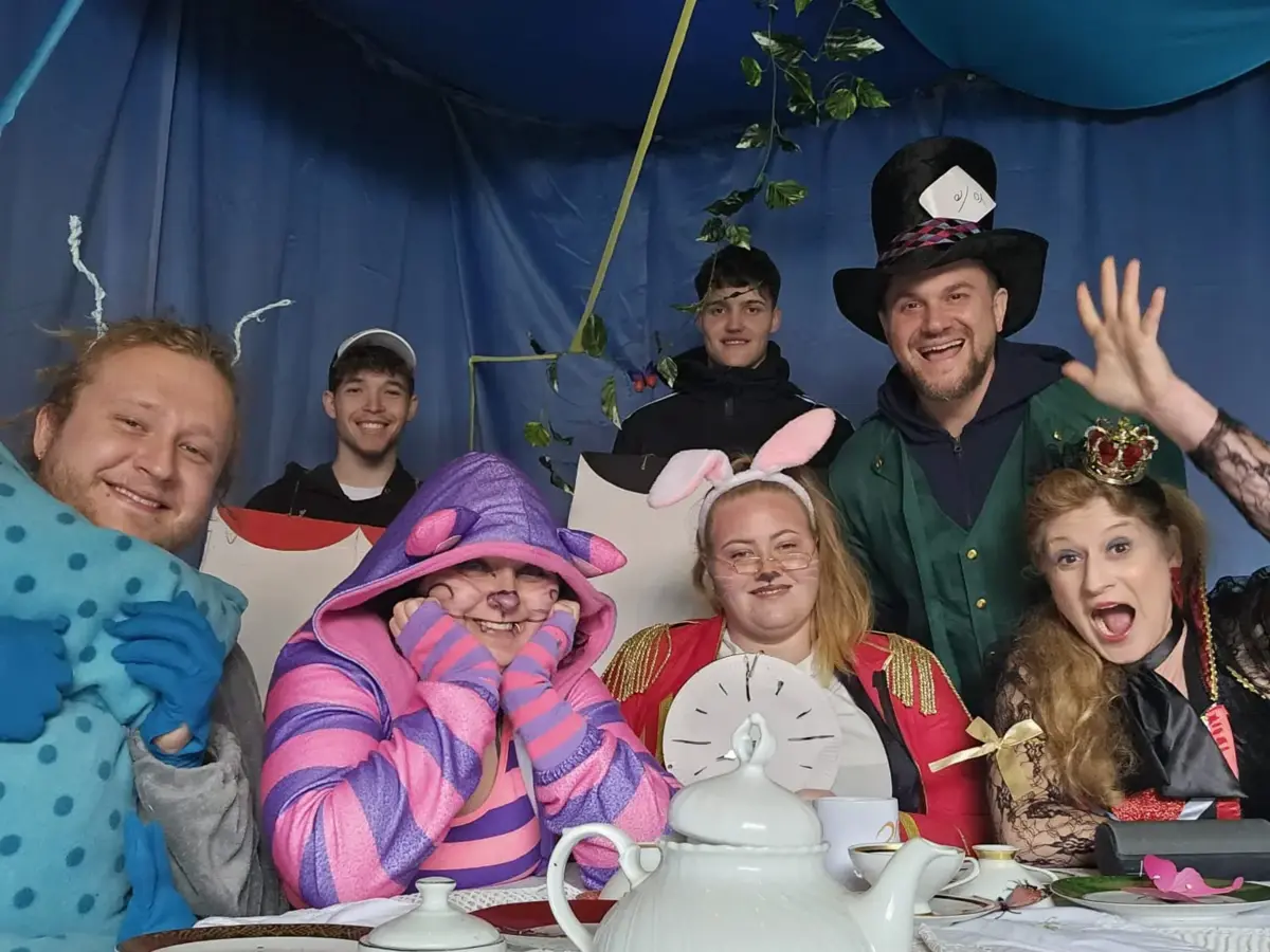 verkleidete Menschen in einem Zelt an einem Tisch mit Teegeschirr