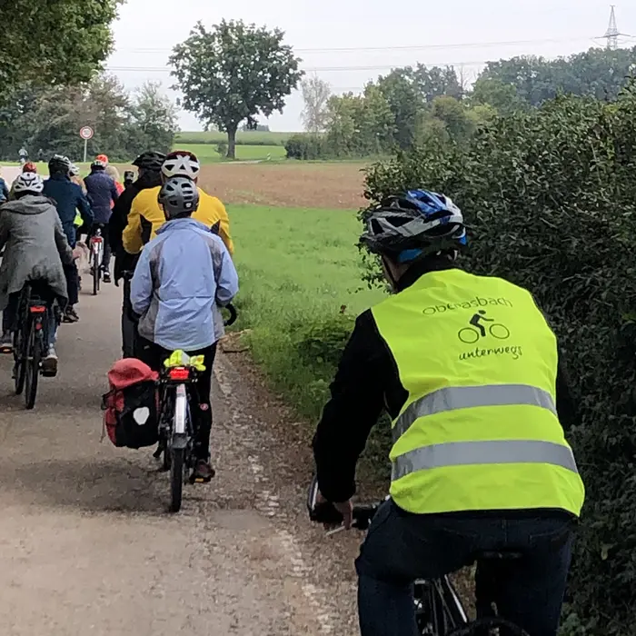 Eine Gruppe von Radfahren auf einem Waldweg. Der rechte Fahrer trägt eine Warnweste mit dem Aufdruck "Oberasbach unterwegs". 