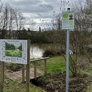 Zwei Schilder vor dem Biotop im Hintergrund.