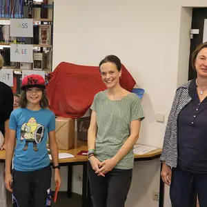 Ein Junge bei der Preisübergabe. Im Hintergrund drei Frauen vom Büchereiteam.