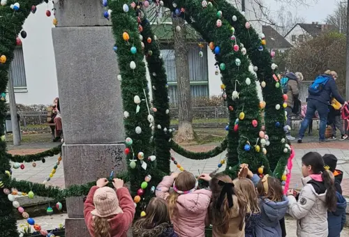 Kinder hängen Eier an einem Osterbrunnen auf 