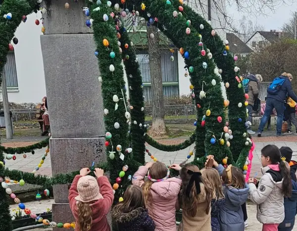 Kinder hängen Eier an einem Osterbrunnen auf 