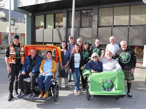 2 E-Rikschas mit Passagieren, dahinter das Team. 